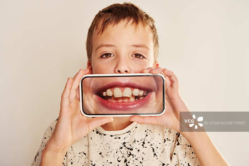 男孩举着一部显示着大笑嘴巴的智能手机图片素材