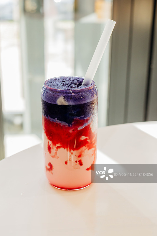 白色桌子上的冰蝶抹茶拿铁和覆盆子冰沙。一杯冰镇夏日饮品。无咖啡因饮品。健康食品概念。图片素材