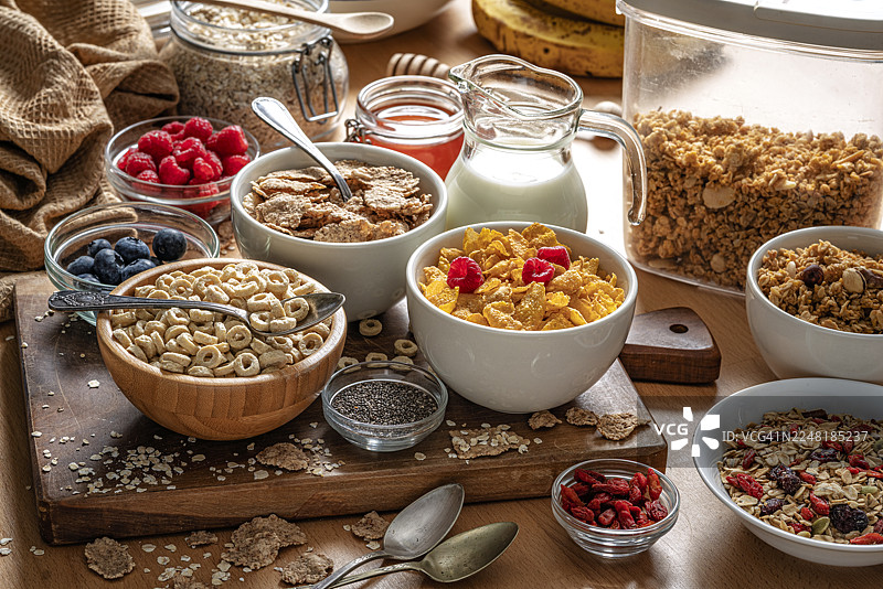 餐桌上摆满了各式各样的早餐谷物。玉米片、什锦麦片、格兰诺拉麦片、奇亚籽和浆果，有益于消化系统健康。富含膳食纤维的食物，有益肠道健康。图片素材