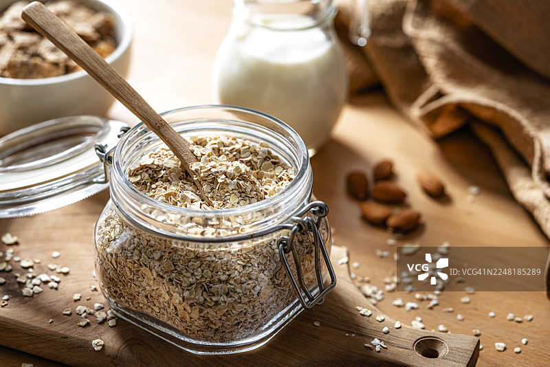 密封的厨房玻璃罐中卷起或压扁的燕麦片，放在早餐桌上。富含膳食纤维的健康食品，有益肠道或消化系统健康。图片素材