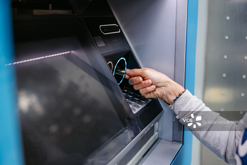 一位成熟的女性在西班牙巴塞罗那的自动取款机上使用信用卡取款图片素材