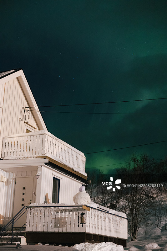 在乡村地区，一位女士在斯堪的纳维亚房屋上空欣赏壮丽的北极光图片素材