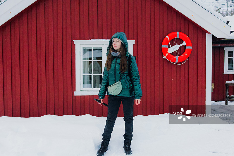 冬季的罗弗敦，一名旅人在渔村里，背景是红色的渔民小屋图片素材