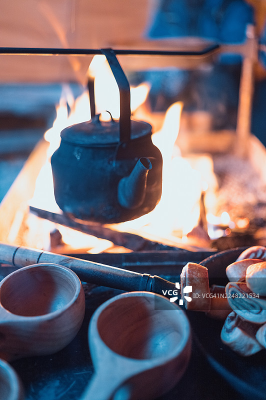 篝火上烧水壶，旁边放着木杯和糕点图片素材