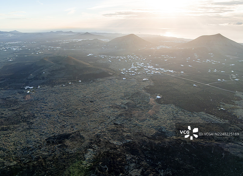 早晨光线下风景如画的火山地貌，包括火山坑和熔岩田，马斯达赫村的白色房屋，火山公园，鸟瞰图，兰萨罗特，加那利群岛，西班牙图片素材