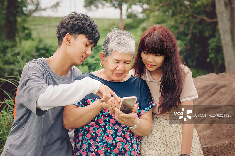 一位年长的女士和她的孙子孙女正在使用手机图片素材