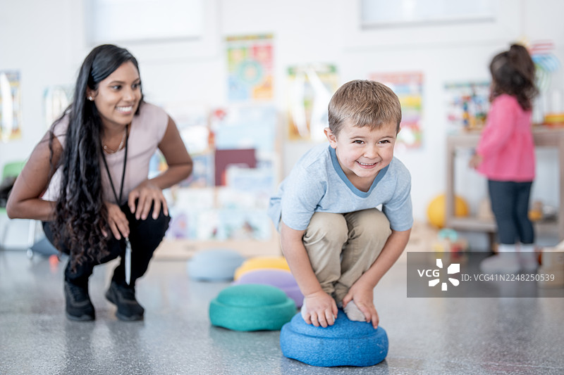 快乐男孩在泡沫垫上玩耍，多元化的老师和同学在一旁指导图片素材