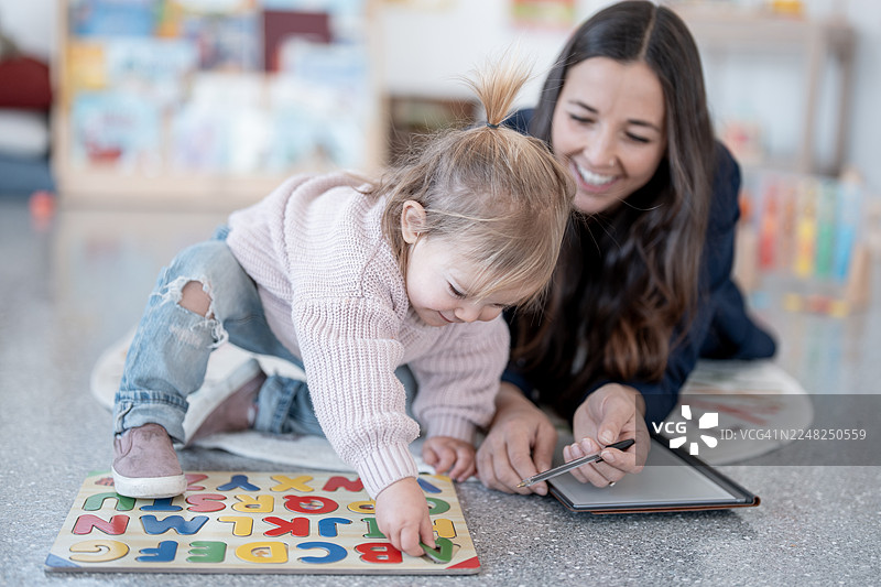 妈妈和女儿在地板上玩字母拼图和学习平板电脑图片素材