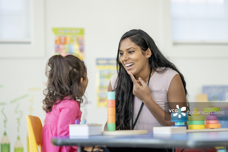 一位西班牙裔教师在色彩丰富的教室里，与一个快乐的孩子一起玩积木和玩具。图片素材