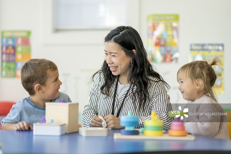 亚裔女教师与快乐的孩子们在教室里玩叠叠乐玩具图片素材