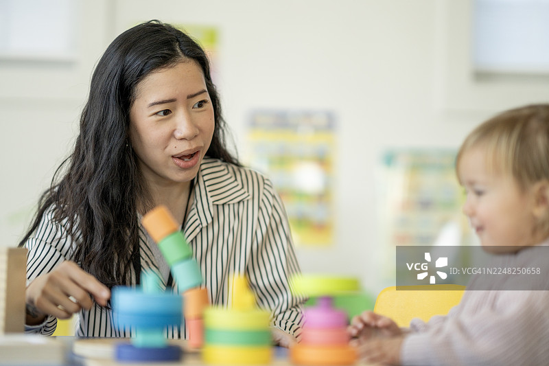 亚洲女教师在明亮的教室里，用色彩鲜艳的堆叠玩具与幼儿进行寓教于乐的互动图片素材