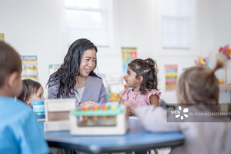 亚裔女教师在寓教于乐的互动中，与快乐的多元文化教室里的孩子们一起玩耍图片素材
