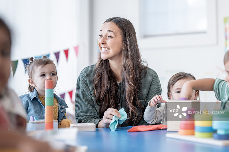 微笑的拉丁裔女老师在色彩丰富的教室里与孩子们互动，进行活动和玩耍图片素材