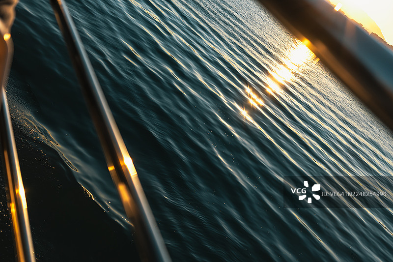 从船甲板栏杆望去，金色落日映照着大海，船尾留下一道轻柔的航迹图片素材