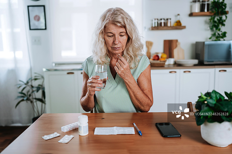 一位年长女性在桌边遵照说明服用药物图片素材