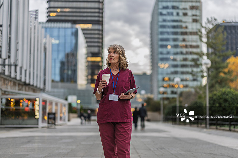 医护人员在城市街道行走，手持咖啡和数码平板电脑图片素材