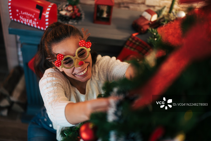 戴着驯鹿眼镜、正在装饰圣诞树的快乐女人图片素材