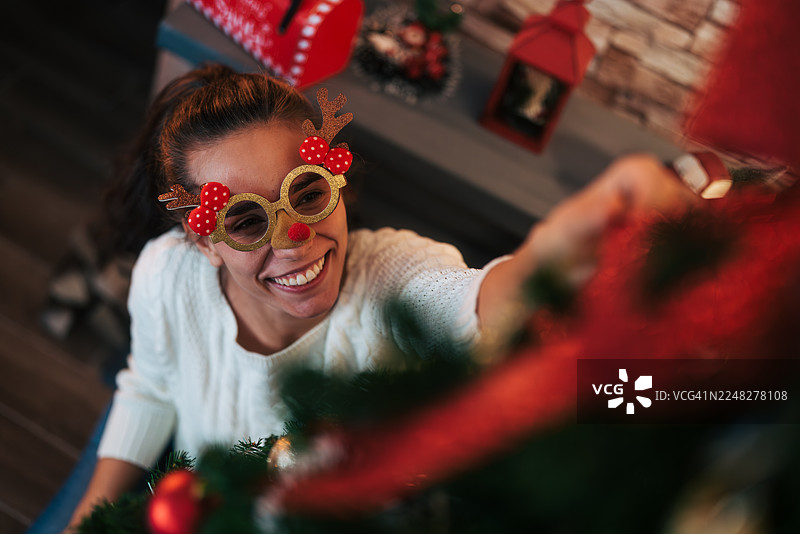 戴着驯鹿眼镜的年轻女子正在装饰圣诞树图片素材