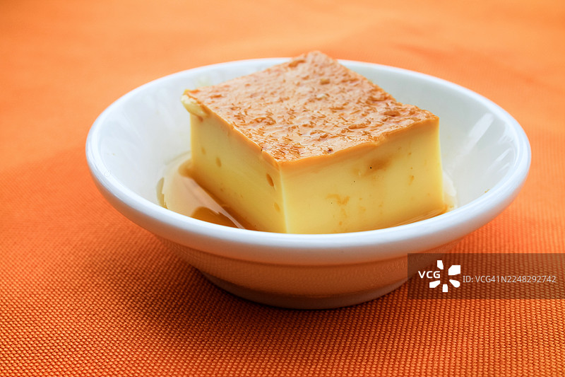 橙色背景上的方形焦糖布丁图片素材