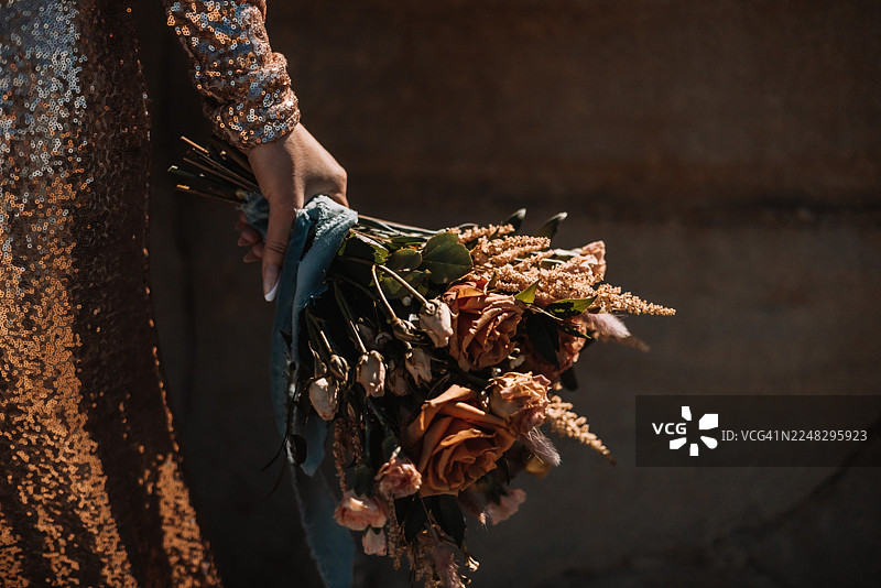 身穿金色亮片连衣裙的女子手持乡村风格花束的温暖特写图片素材