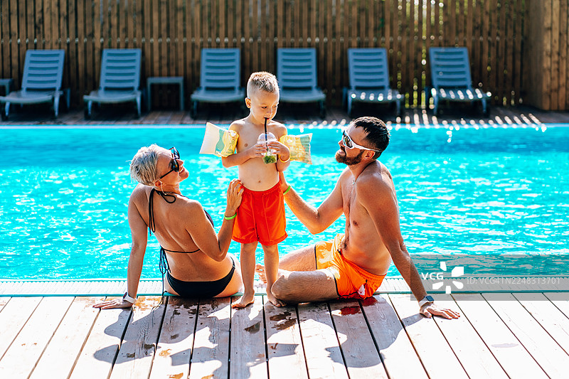 一家人在泳池边放松，孩子在夏日假期里饮用清爽的饮料图片素材