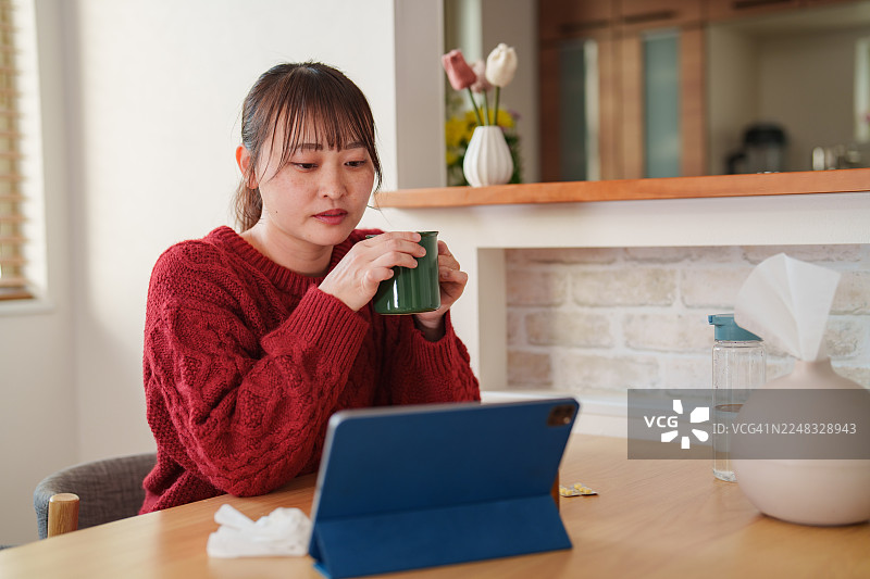 生病的女士在家中进行线上医生咨询时喝热茶图片素材
