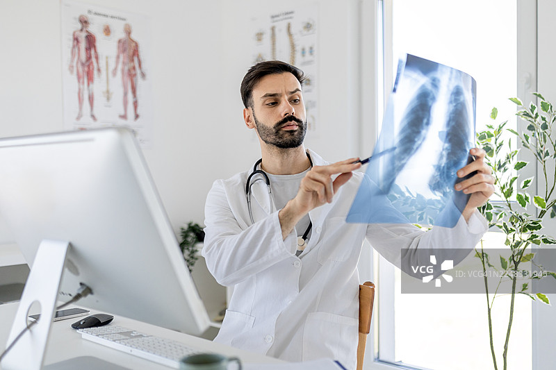 一位严肃的年轻医生正在分析人肺部X光片图片素材
