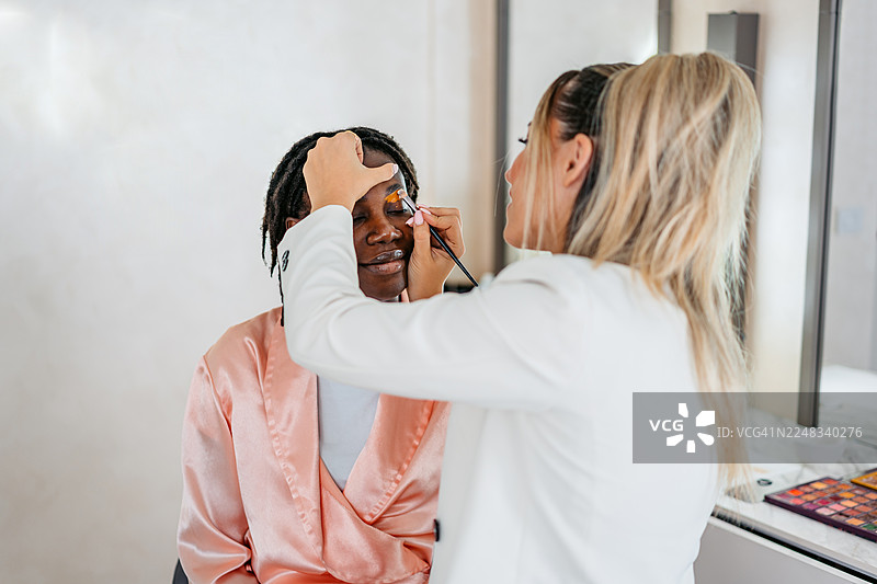 美容师在美容院为年轻的黑人女顾客用遮瑕膏修饰眉毛图片素材