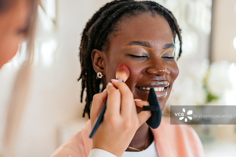 一位女性美容师在美容院为一位年轻的黑人女性顾客上腮红图片素材