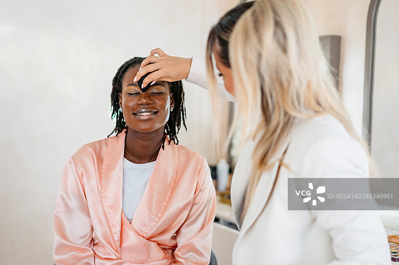美容师在美容院为年轻的黑人女性客户上粉底图片素材