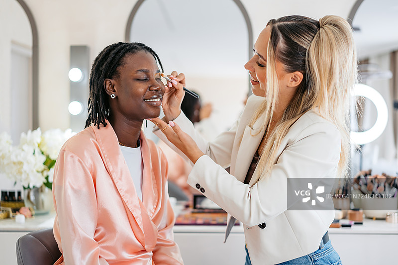 美容师在美容院为年轻的黑人女性顾客用遮瑕膏修眉图片素材