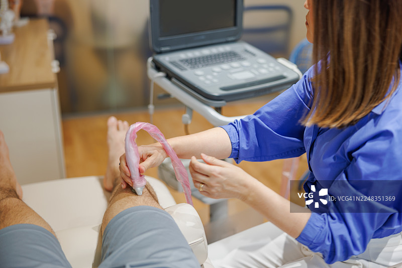 在诊室里，一名女性超声技师正在为患者的膝盖进行超声检查。图片素材