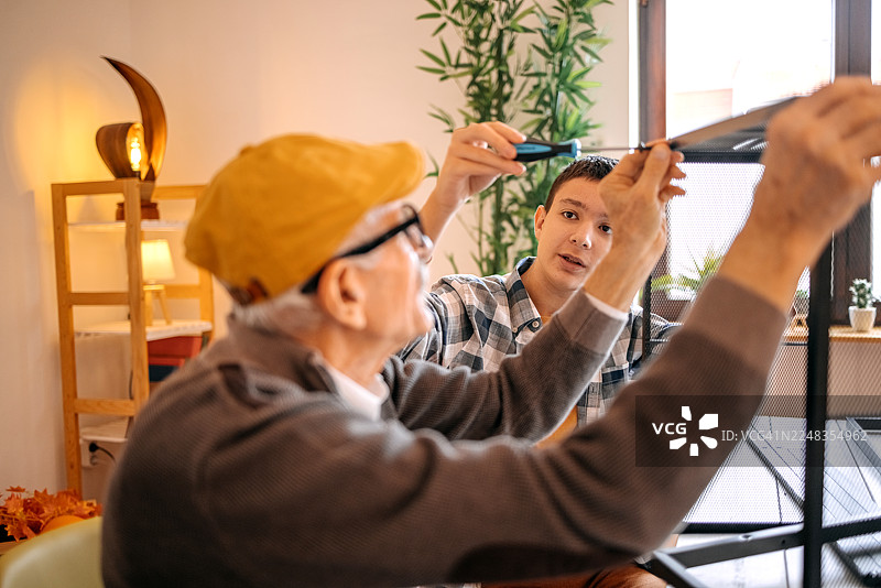 年长的成年男子在家中与十几岁的孙子一起组装新架子图片素材