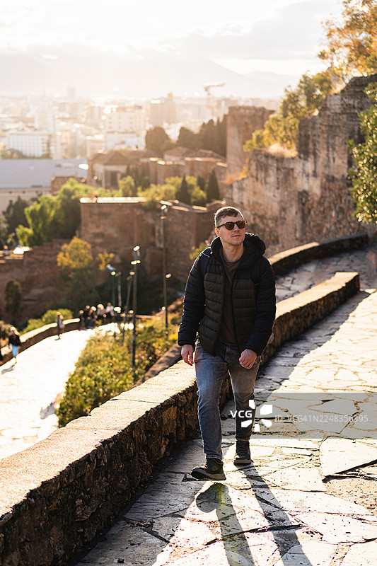 西班牙马拉加：日落时分，男子沿着石板路漫步，远眺城市景色，户外图片素材