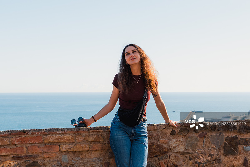 一位女士在石砌露台上欣赏风景如画的海岸城市景观，背景是港口和大海。图片素材