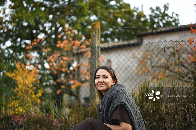 一位女士在秋天的自然环境中微笑，背景有篱笆图片素材