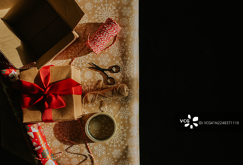 正在包装中的圣诞礼物，周围散落着包装纸和红白麻绳图片素材