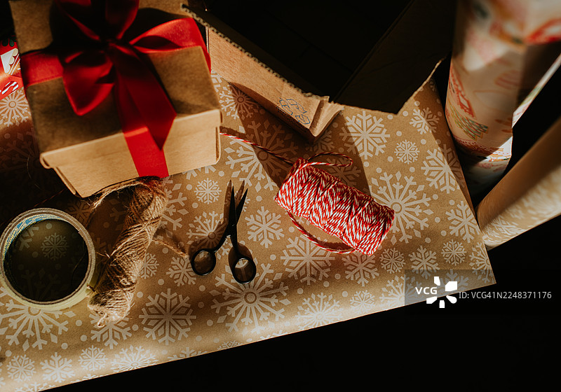 正在包装中的圣诞礼物，周围散落着雪花图案的包装纸、胶带以及红白相间的麻绳图片素材