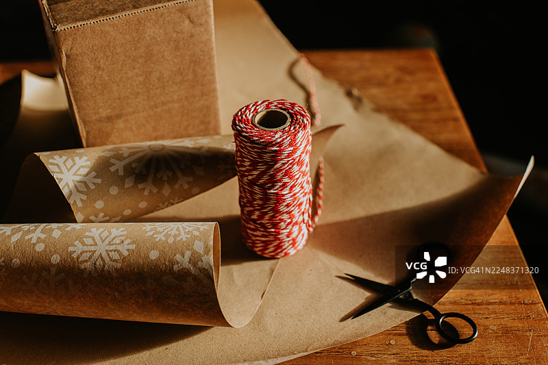 红白相间的麻绳放在圣诞包装纸上，包装纸在木桌上，旁边放着一把小剪刀。图片素材