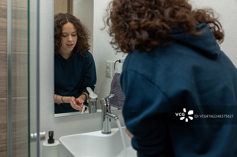 少女在浴室的水槽里洗手，体现了日常的卫生习惯和个人护理。图片素材