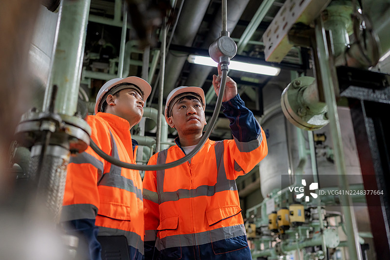 两位身穿防护服的工程师在生产线上检查管道和机器阀门，讨论储罐、石油生产平台和炼油系统在设计改进和运行效率方面的问题。图片素材