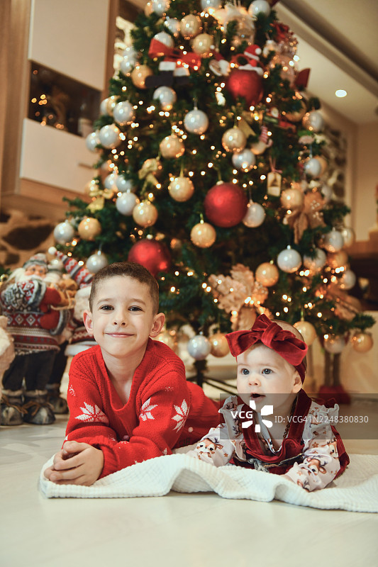 温馨室内场景，装饰好的圣诞树旁，兄妹（或姐弟）欢乐的圣诞家庭合影图片素材