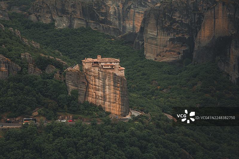 希腊梅特奥拉，一座修道院坐落于高耸的岩石柱上，周围环绕着葱郁的绿色森林和悬崖图片素材