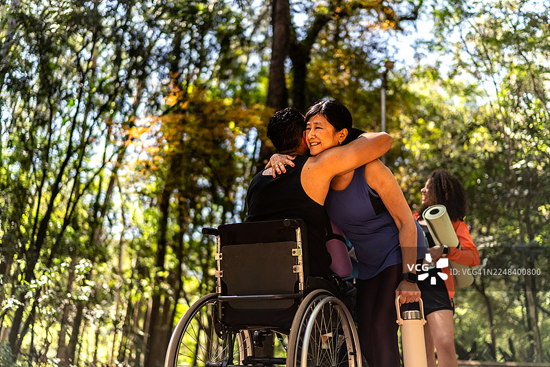 一位成熟的女性在公园里向坐轮椅的朋友打招呼图片素材