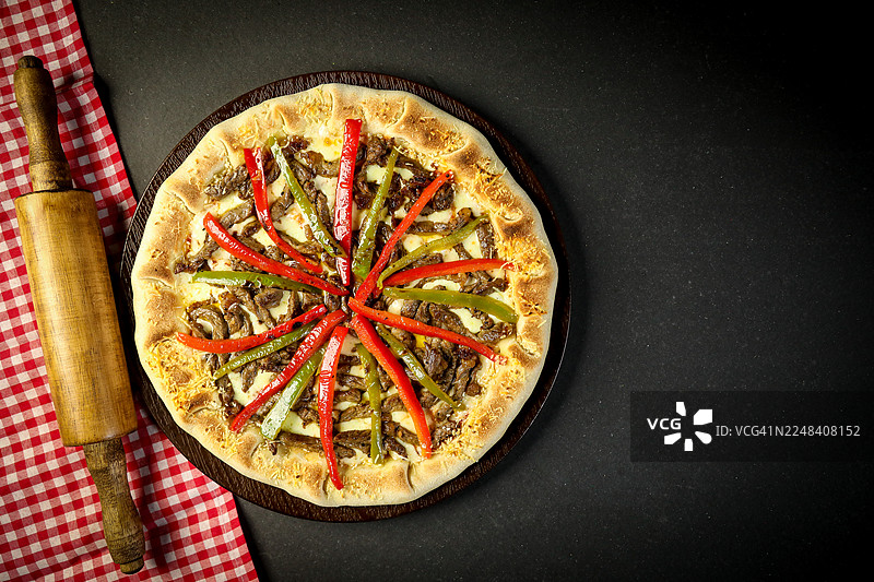 深色背景下的披萨，木桌上摆放着香料。图片素材