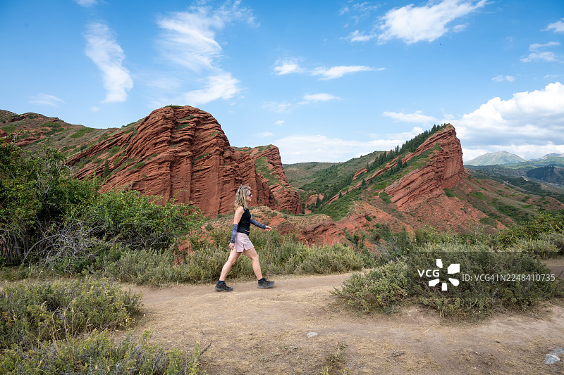 快乐的女旅行者走在著名的杰蒂奥古兹峡谷（七公牛岩）的条纹红色砂岩悬崖前。 探险和积极的生活方式。图片素材
