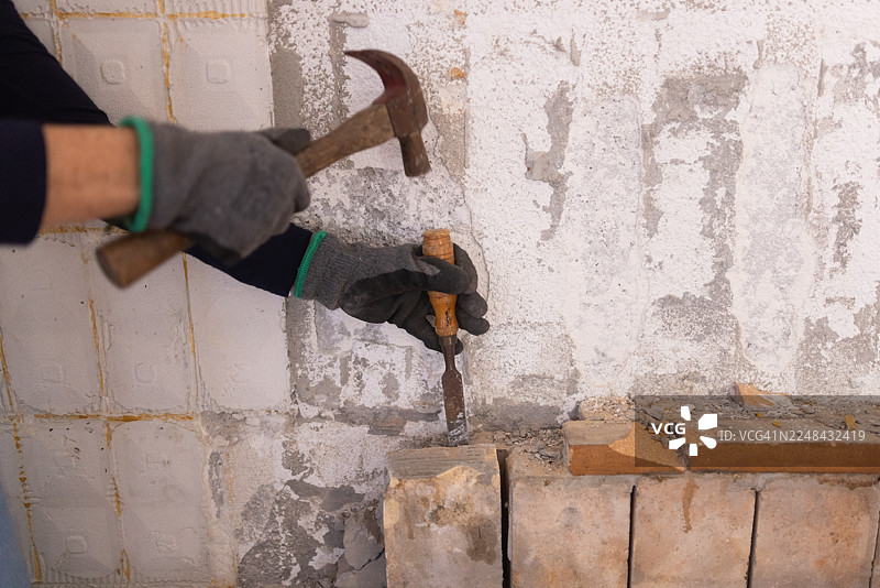 翻新期间，戴手套的女子用锤子和凿子敲掉旧砖的特写图片素材
