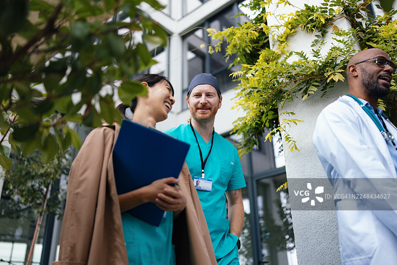 医疗团队在现代医院大楼附近进行户外交流，展现出专业精神和友好氛围图片素材