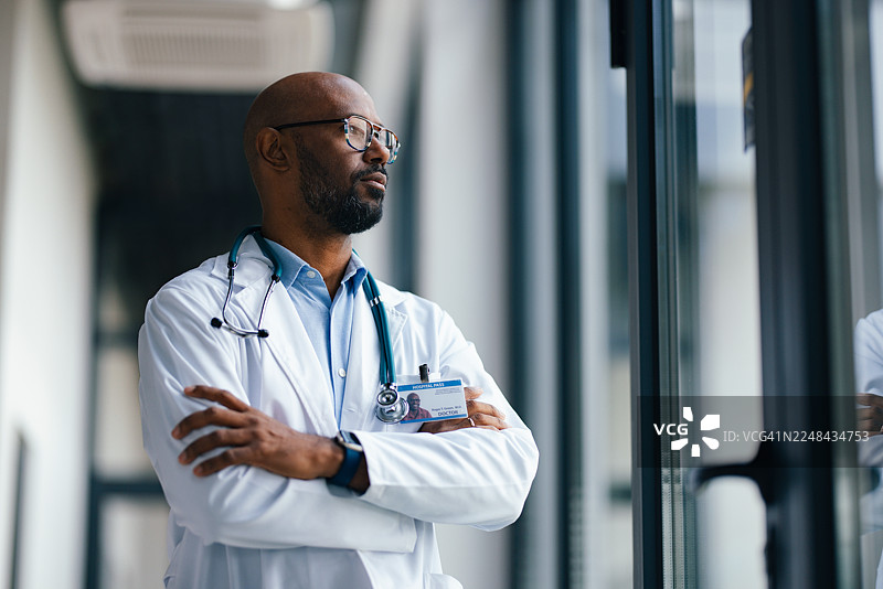 一位穿着白大褂、双臂交叉、充满自信的医生站在医院走廊里图片素材