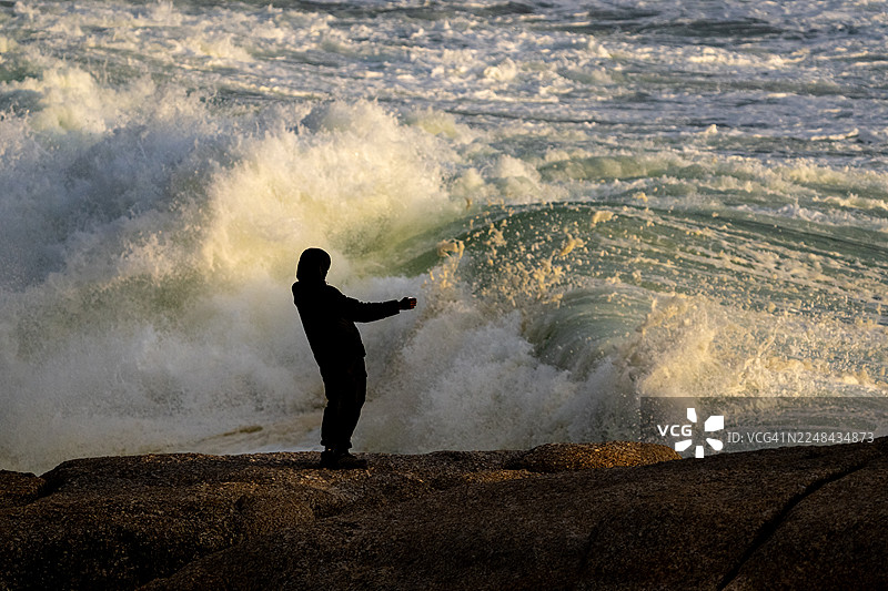 海浪汹涌拍打，一人正在挥手示意。图片素材